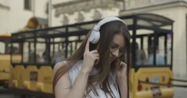 Gözlüklü çekici kız şehirde dolaşıyor ve kulaklıklarıyla müzik dinliyor.