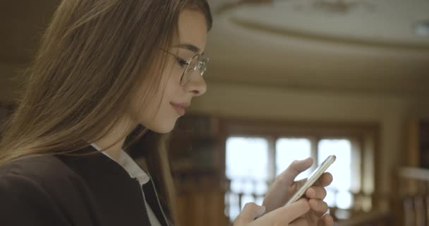 Kvinnlig student, bibliotekets plats. Charmig flicka slappnar av lyssna på musik i sina hörlurar — Stockvideo
