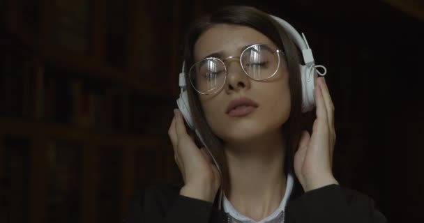 Kvinnlig student, bibliotekets plats. Charmig flicka slappnar av lyssna på musik i sina hörlurar — Stockvideo