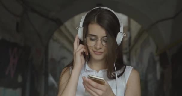 Чарівна дівчина в окулярах гуляє по місту і слухає музику в її навушниках — стокове відео