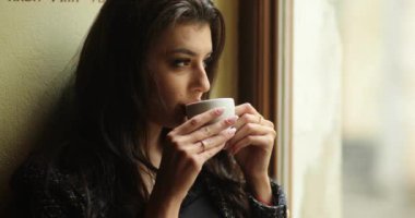 4 bin. Şehirdeki kadın. Çekici kadın manken kollarında bir fincan kahve tutuyor ve kafeteryada otururken uzaklara bakıyor.