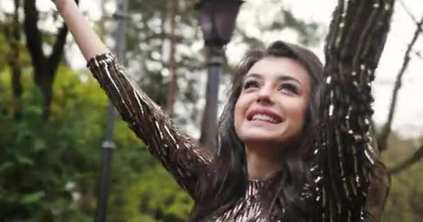 4k. Una mujer en la ciudad. modelo atractiva en vestido de noche brillante camina a lo largo del paso en el parque de otoño y sacude su pelo largo morena — Vídeos de Stock