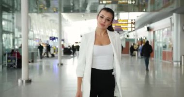 4 bin. Yavaş ve hızlı çekim. Siyahlar içinde beyaz elbiseli genç bir iş kadını uluslararası havaalanının koridorunda yürüyor.