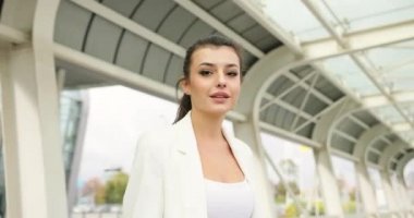 4 bin. Yavaş ve hızlı çekim. Süslü giyinmiş, siyah beyaz elbiseli genç bir iş kadını modern cam bir binanın önünde yürüyüp saçlarını sallıyor.