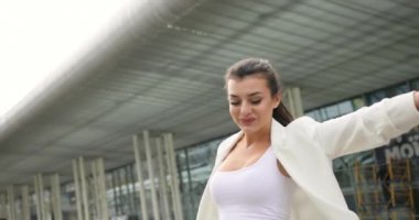 4 bin. Yavaş ve hızlı çekim. Süslü giyinmiş, siyah beyaz elbiseli genç bir iş kadını modern cam bir binanın önünde yürüyüp saçlarını sallıyor.