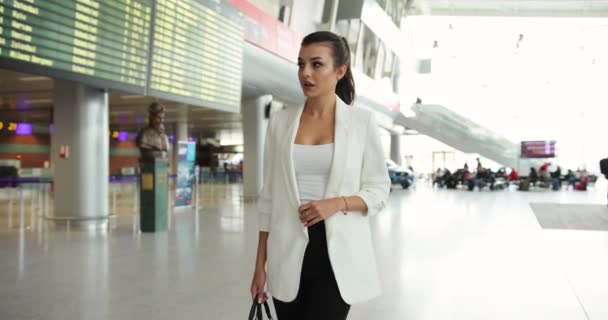 4k. Movimento lento e rápido. Fantasia vestida jovem mulher de negócios em roupas pretas e brancas caminha através do salão do aeroporto internacional — Vídeo de Stock