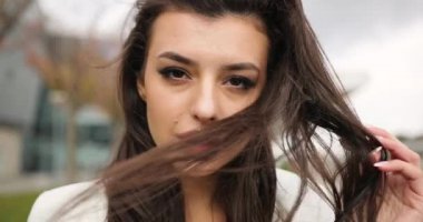 4 bin. Yavaş ve hızlı çekim. Süslü giyinmiş, siyah beyaz elbiseli genç bir iş kadını modern cam bir binanın önünden geçiyor, arkasını dönüyor, saçını sallıyor ve doğruca geçide bakıyor.