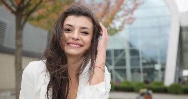 4 bin. Yavaş ve hızlı çekim. Süslü giyinmiş, siyah beyaz elbiseli genç bir iş kadını modern cam bir binanın önünden geçiyor, arkasını dönüyor, saçını sallıyor ve doğruca geçide bakıyor.