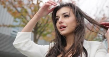 4 bin. Yavaş ve hızlı çekim. Süslü giyinmiş, siyah beyaz elbiseli genç bir iş kadını modern cam bir binanın önünden geçiyor, arkasını dönüyor, saçını sallıyor ve doğruca geçide bakıyor.