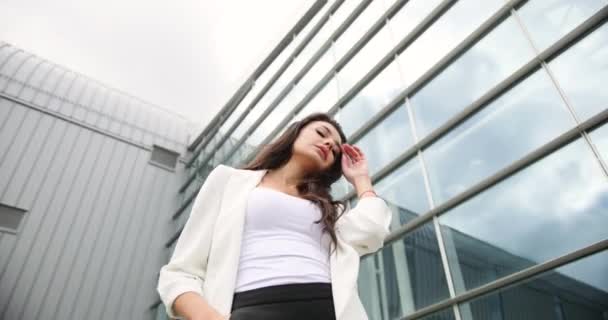 4k. Zeitlupe und Zeitraffer. Phantasievoll gekleidete junge Geschäftsfrau in schwarz-weißer Kleidung posiert vor einem modernen Glasgebäude im Freien — Stockvideo