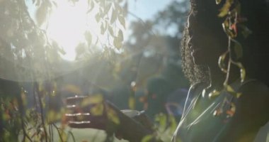 Güzel Afro-Amerikan Kız Parlak Gülümseyen Doğal Kıvırcık Saçlar Yeşil Plastik Tetik Spreyi Açık Hava Bitkileri Güneş Işığı 4k Yavaş Hareket Doğa.