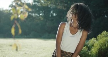Sevimli Afro-Amerikalı kız, büyüleyici gülüşü ve yeşil göz gölgeleri kulaklıktaki müzik yüzünden enerjik bir şekilde dans ederken kıvırcık saçlarını ve ellerini sallıyor. Açık havada portre.