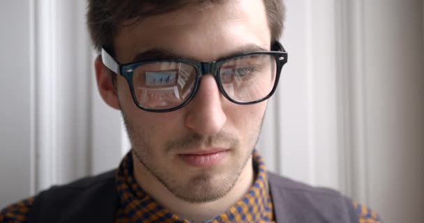 Giovane uomo d'affari esausto sta digitando e lavorando sul computer portatile. Il riflesso dei diagrammi e della grafica nei suoi occhiali. Ritratto ravvicinato. 4k. — Video Stock
