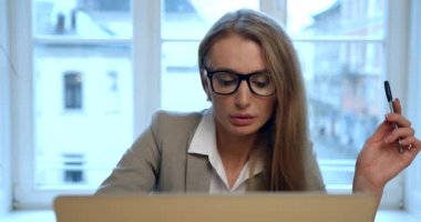 Bilgisayarda çalışan ve bir şeyler yazan, gözlüklü, yoğun, güzel iş kadınının ön görüntüsü. İş yeri. 4k.