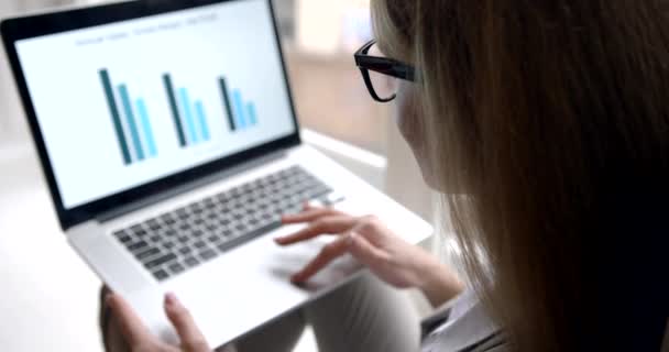 Vedere din spate a femeii de afaceri blonde cu ochelari care lucrează cu grafică de afaceri și diagrame folosind laptopul. 4k . — Videoclip de stoc