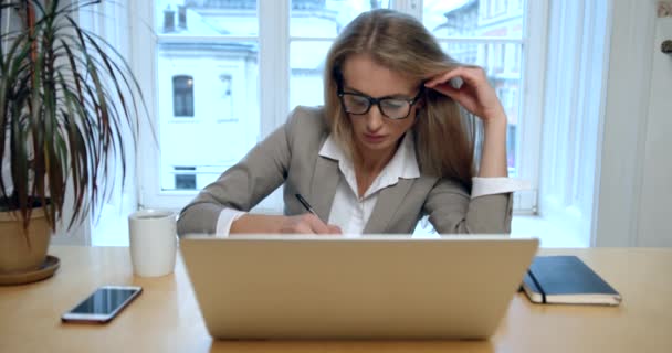 피곤하고 긴장 한 금발 여성 이 안경을 벗고 직장에서 차를 마시는 것 보다 뭔가를쓰고 노트북을 만들고 있습니다.. — 비디오