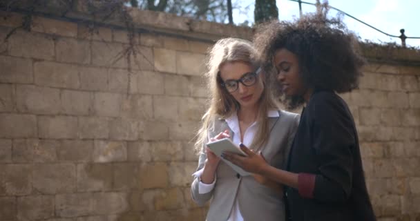 Twee lachende multi-race zakenvrouwen gebruiken tablet buiten. — Stockvideo