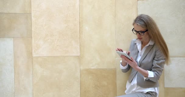 Portret van de jonge blonde zakenvrouw bedachtzaam en verrast tijdens het gebruik van de tablet aan de gele muur. — Stockvideo
