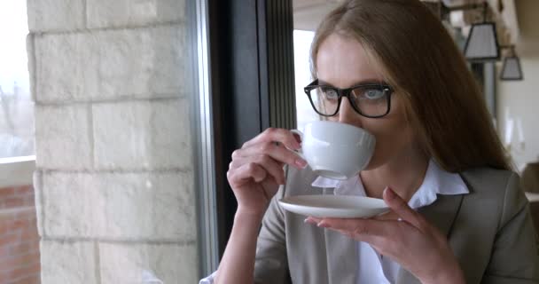 Die attraktive blonde Geschäftsfrau mit Brille genießt ihren Kaffee im Café. Innenporträt in Großaufnahme. — Stockvideo