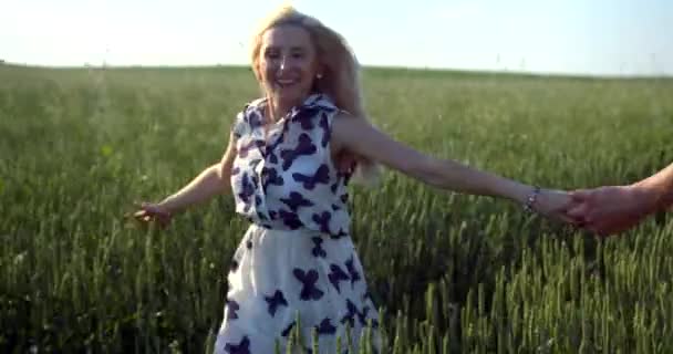 Retrato de cerca de la joven sonriente con maquillaje natural sosteniendo la mano de su novio mientras corre por el campo con ruedas verdes. — Vídeos de Stock