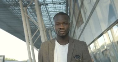 Güneşli caddede ilerlerken kameraya bakan kendinden emin Afrikalı bir adam. 4K görüntü. Yakın plan portre.