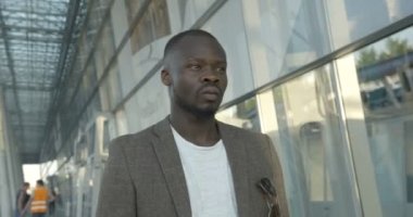 Yan portre. Kendine güvenen, şık giyinmiş Afro-Amerikan bir adam güneşli cadde boyunca yürüyor ve yana dönüyor. 4k görüntü.