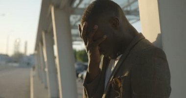 Genç Afrikalı bir adamın başı dertte. Üzgün adamın ciddi sorunları var ve dışarıda acı çekiyor. Olumsuz duygu ifadesi. 4k görüntü.