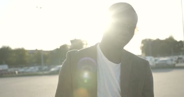 Gros plan portrait de l'homme afro-américain sérieux élégant avec des lunettes de soleil toucher ses cheveux tout en allant vers l'avant à la caméra dans les lits de soleil. Images 4k. — Video