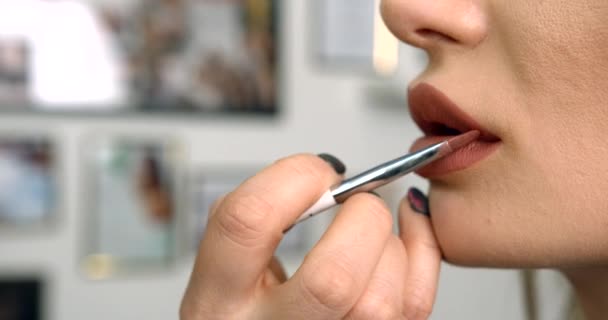 Vista lateral de cerca de la mano del maquillador aplicando el lápiz labial beige usando el pincel en la boca del modelo. — Vídeo de stock