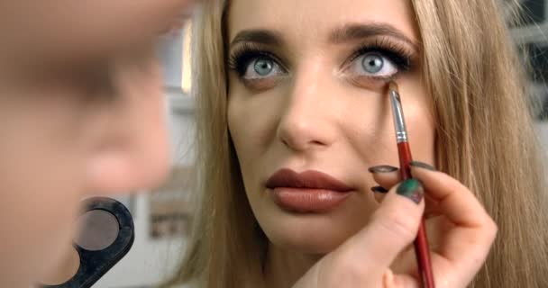 Maquillaje profesional artista está haciendo los ojos maquillaje para la encantadora modelo rubia. Primer plano. 4k. — Vídeo de stock