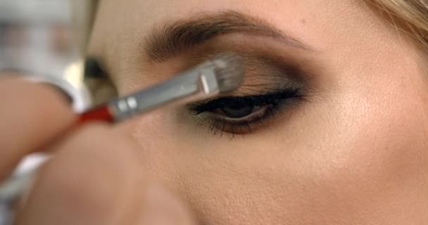 Professionelle Visagistin verwendet den Pinsel, um die Kosmetik auf den Modelaugen aufzubringen. Seitenansicht aus nächster Nähe. — Stockvideo