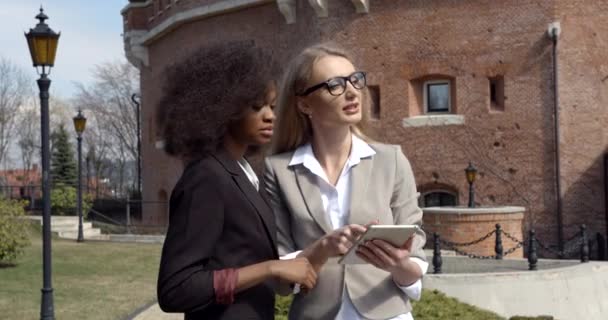 De blonde blanke afro-Amerikaanse zakenvrouw laat iets zien op de tablet en buiten aan de afro-Amerikaanse collega. — Stockvideo