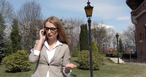 Sinirli sarışın iş kadını aktif olarak cep telefonuyla tartışıyor. Açık havada portre. — Stok video
