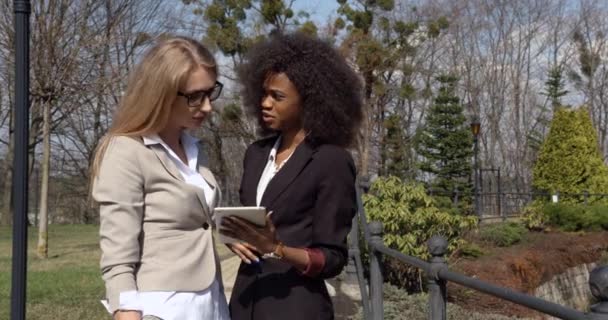 Afro-Amerikaanse en blanke vrouwelijke collega 's behandelen het probleem met behulp van de tablet. Buiten locatie. Halve lengte portret. — Stockvideo