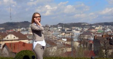 Gözlüklü genç sarışın iş kadınının yarım boy portresi manzaranın arka planında cep telefonuyla mutlu bir şekilde konuşuyor..