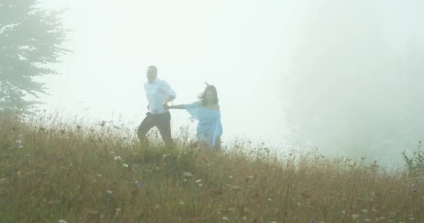 Una pareja feliz corre por el campo durante la niebla. El hombre está dando vueltas alrededor de la hermosa mujer alegre. — Vídeos de Stock