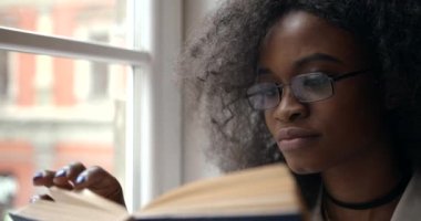 Pencere kenarında oturan bir kitap okuma ile oldukça Afro-Amerikan kız