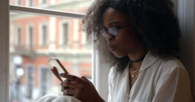 Gözlüklü, gülümseyen Afro-Amerikan kadın cep telefonuyla sohbet ediyor ve komik bir mesaj alıyor. Yakın plan portre.