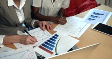 Ofisteki grafikler ve diyagramlar üzerinde çalışan iki çok kültürlü iş kadınının ellerinin yakın çekim görüntüsü..