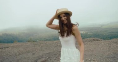 Beyaz yaz elbisesi ve dağın tepesinde koşan hasır şapkalı çekici genç bayana arkadan bak.