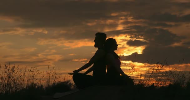 Ζευγάρι κάθεται πίσω στην πλάτη σε lotus γιόγκα θέση στην ύπαιθρο, ενώ το ηλιοβασίλεμα. — Αρχείο Βίντεο