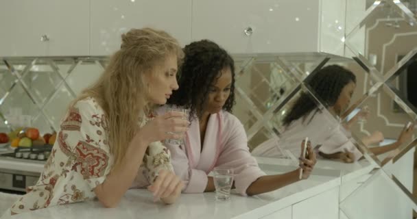 여자 친구 두 명의 아침 사진. 분홍색 옷을 입은 아프리카 소녀가 휴대폰으로 웃고 있는 금발 친구에게 무언가를보여 주고 있습니다.. — 비디오