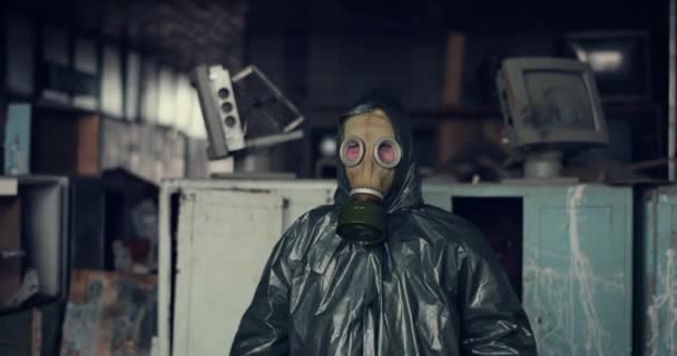 Emoção humana em roupas especiais com máscara de gás. um homem com uma capa de chuva e uma máscara de gás se esconde na sala destruída, levanta as mãos e grita — Vídeo de Stock