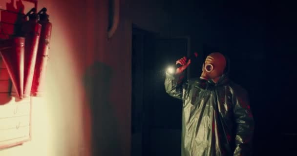 Людина в газовій масці проходить біля пожежної підставки і світить на нього ліхтарик — стокове відео