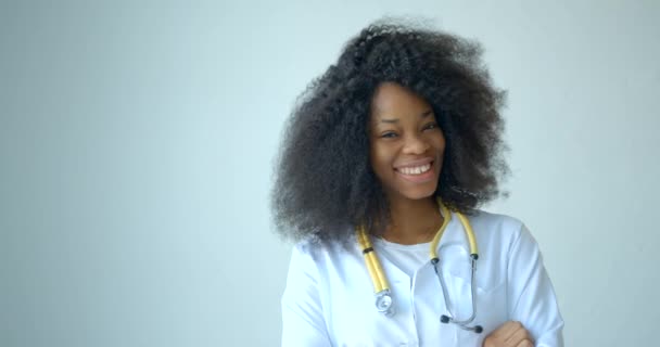 Retrato del encantador médico africano feliz sonriendo y mirando a cámara en el fondo blanco. La mujer lleva la bata y el estetoscopio. Imágenes de 4k. — Vídeos de Stock