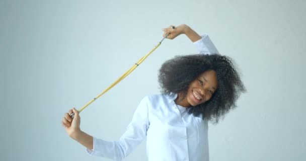 Portret van de jonge mooie Afrikaanse vrouw in doktersjas met mooie glimlach spelen met de stethoscoop op de witte achtergrond. — Stockvideo