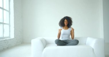 Gündelik giysiler içinde genç ve çekici bir Afrikalı kadın nilüfer çiçeği pozuyla beyaz izole bir odada yoga yapıyor. 4k görüntü.