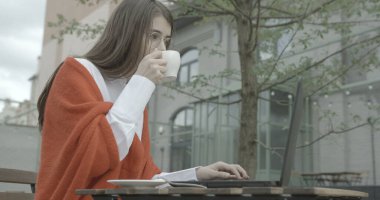 Gözlüklü çekici esmer, çalışırken kahve içiyor. Çalışırken ve dışarıda laptopta sohbet ederken. 4k görüntü.