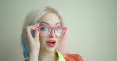 Parlak makyajlı, pembe gözlükler takan ve beyaz arkaplanda hava öpücüğü gönderen güzel sarışın kadının portresi. Kadının pembe ve mavi göz farları var ve...