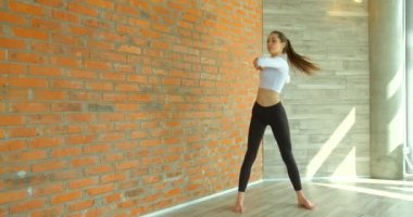 Spor giysili, uzun boylu esmer kızın, kollarını ve sırtını esnetirken, tuğla duvara yaslanırken ve yere eğildiğinde..
